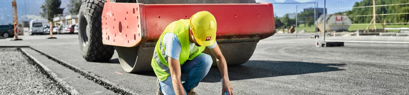 Mann sprayed Markierungen auf den Asphalt vor einer Walze 3