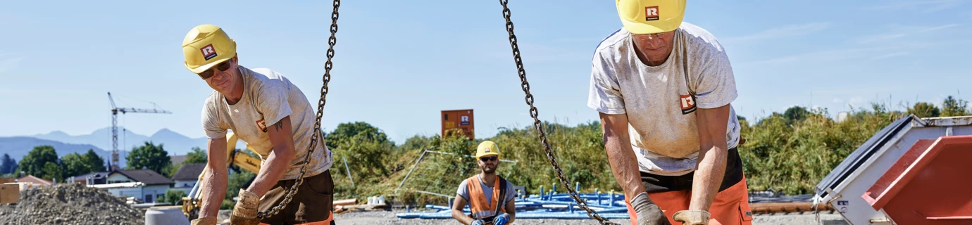 Bauarbeiter stehen auf noch zu gießendem Fundament und laden etwas vom Kran ab