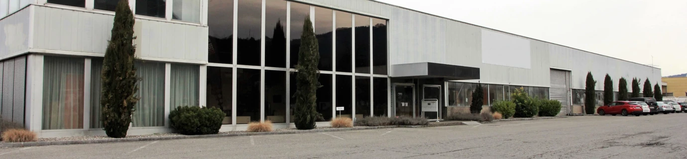 Langes, modernes Bürogebäude und Lagerhalle mit großen Fenstern an einem bewölkten Tag, davor ein Parkplatz mit Autos (Froschweg).