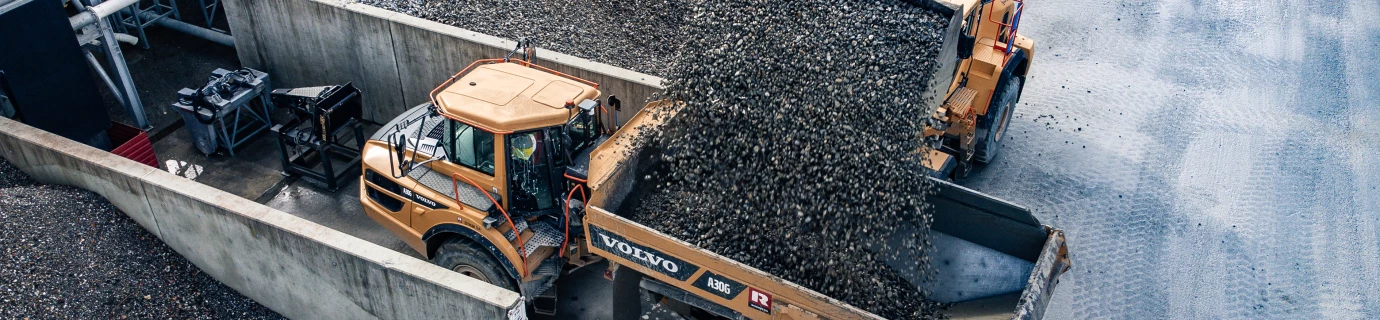 Ein gelber Volvo Radlader bewegt Schotter in einen gelben Volvo Lkw (Steinbruch).
