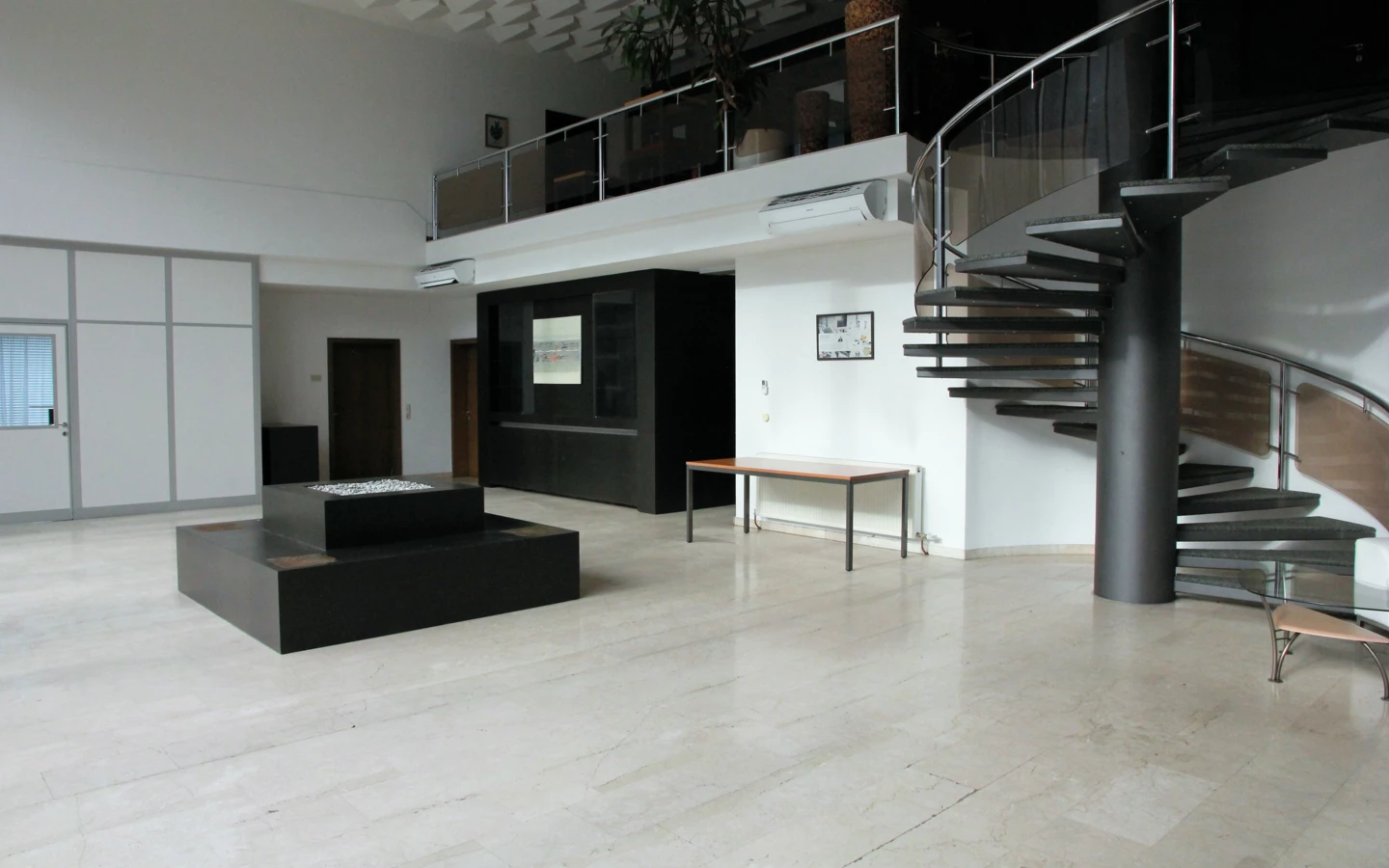 Modernes Bürointerieur mit hellem Marmorboden, einer Wendeltreppe zum Obergeschoss und einer Bar im Hintergrund (Froschweg, Büro).