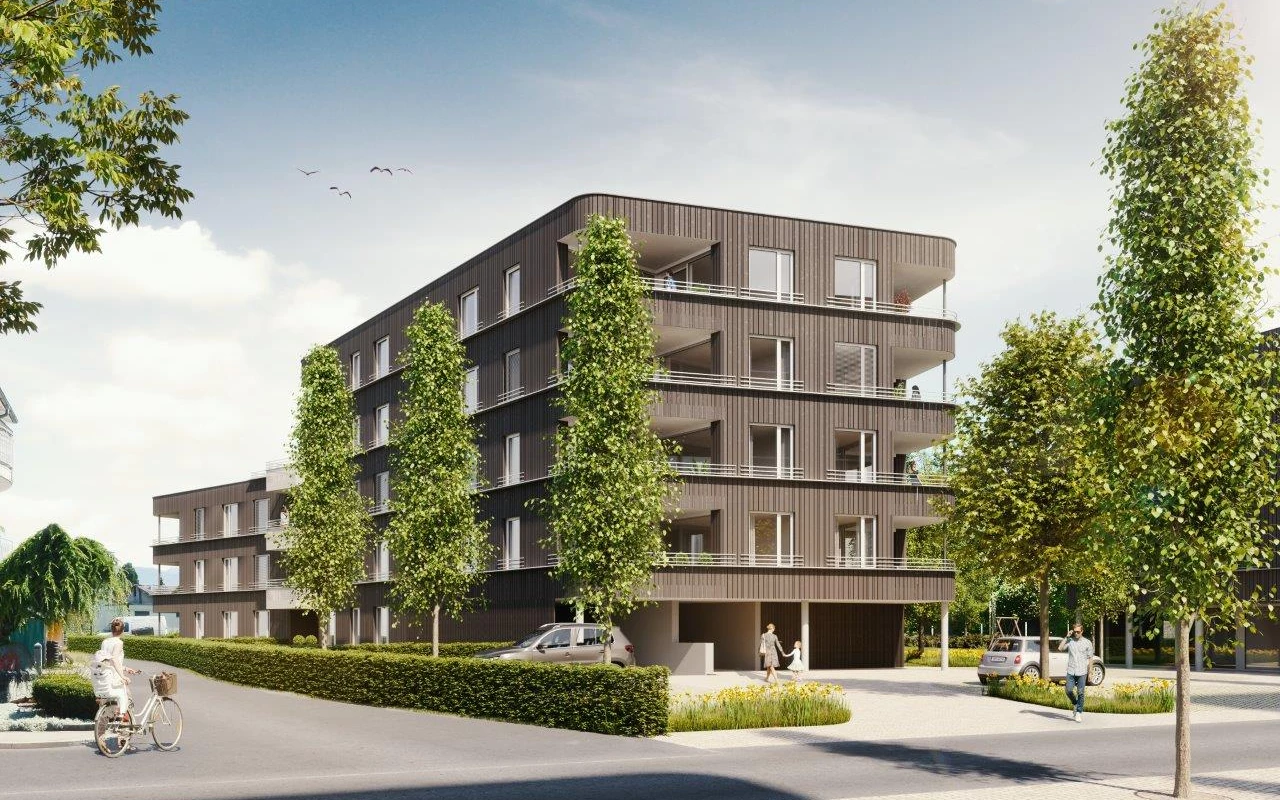 Modernes Wohngebäude Rheindorf mit Balkonen, umgeben von Bäumen und Hecken, Menschen gehen entlang einer Einfahrt.