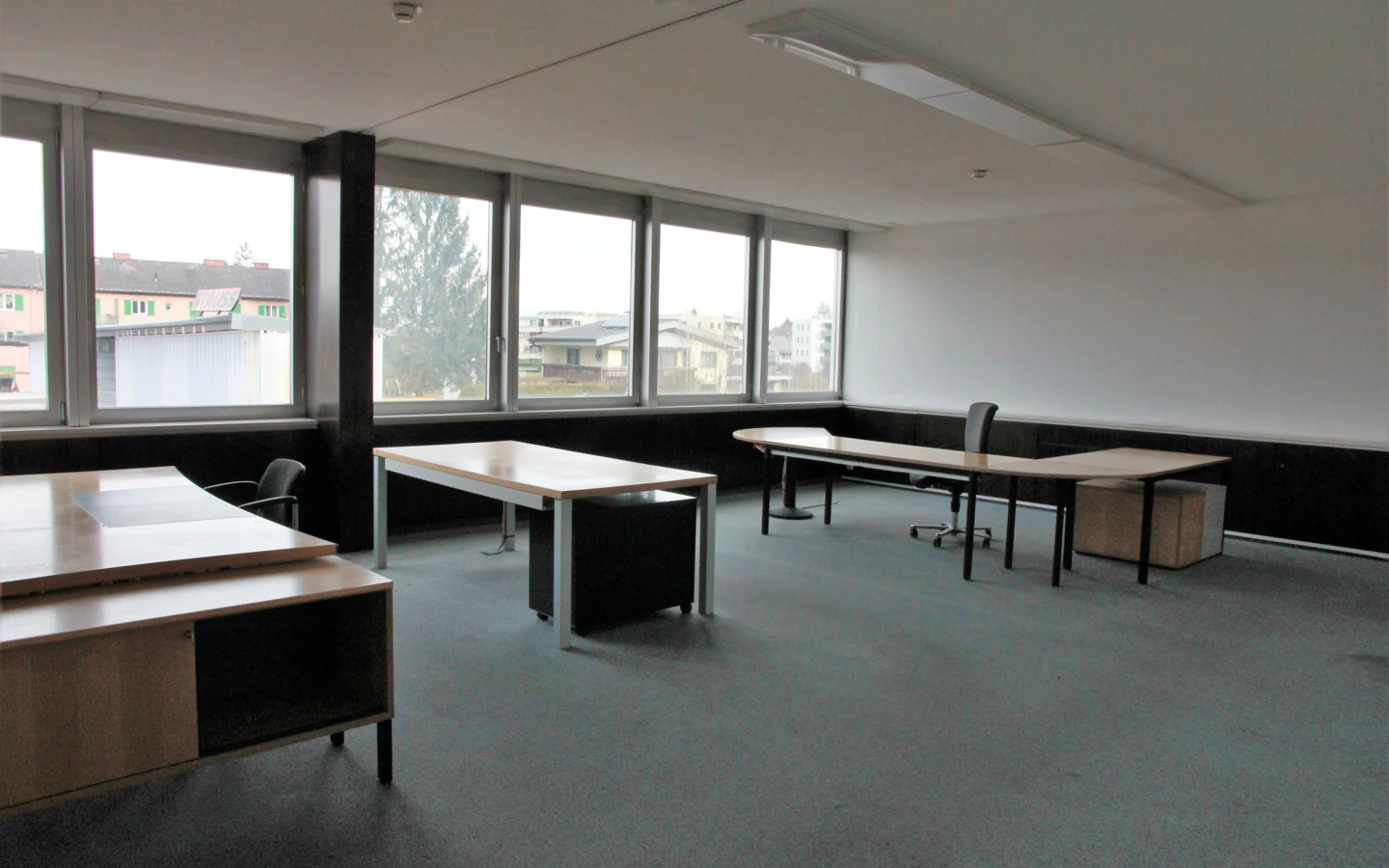 Leeres Büro mit Schreibtischen, Stühlen und einer Fensterfront, die eine Ansicht auf Gebäude und Bäume bietet (Froschweg).