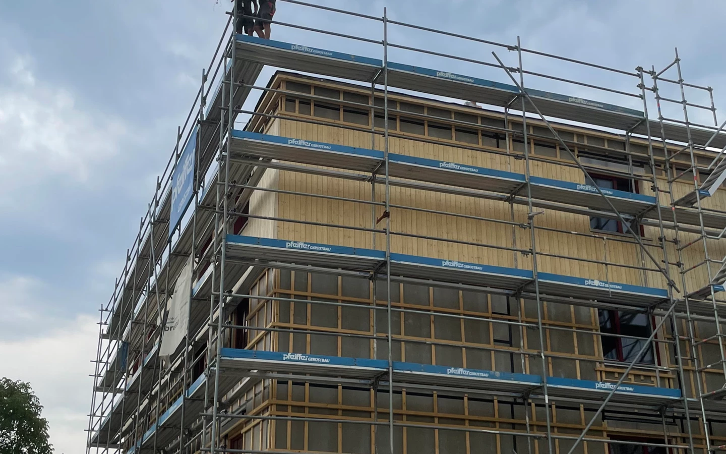 Holz auf Holz: Zwei Zimmerer von Sutter Holzbau beim Stellen des Firstbaums für den Neubau in der Neubaugasse, Lauterach. Darunter ist die Holzfassade sehr gut zu erkennen, die aktuell montiert wird.

