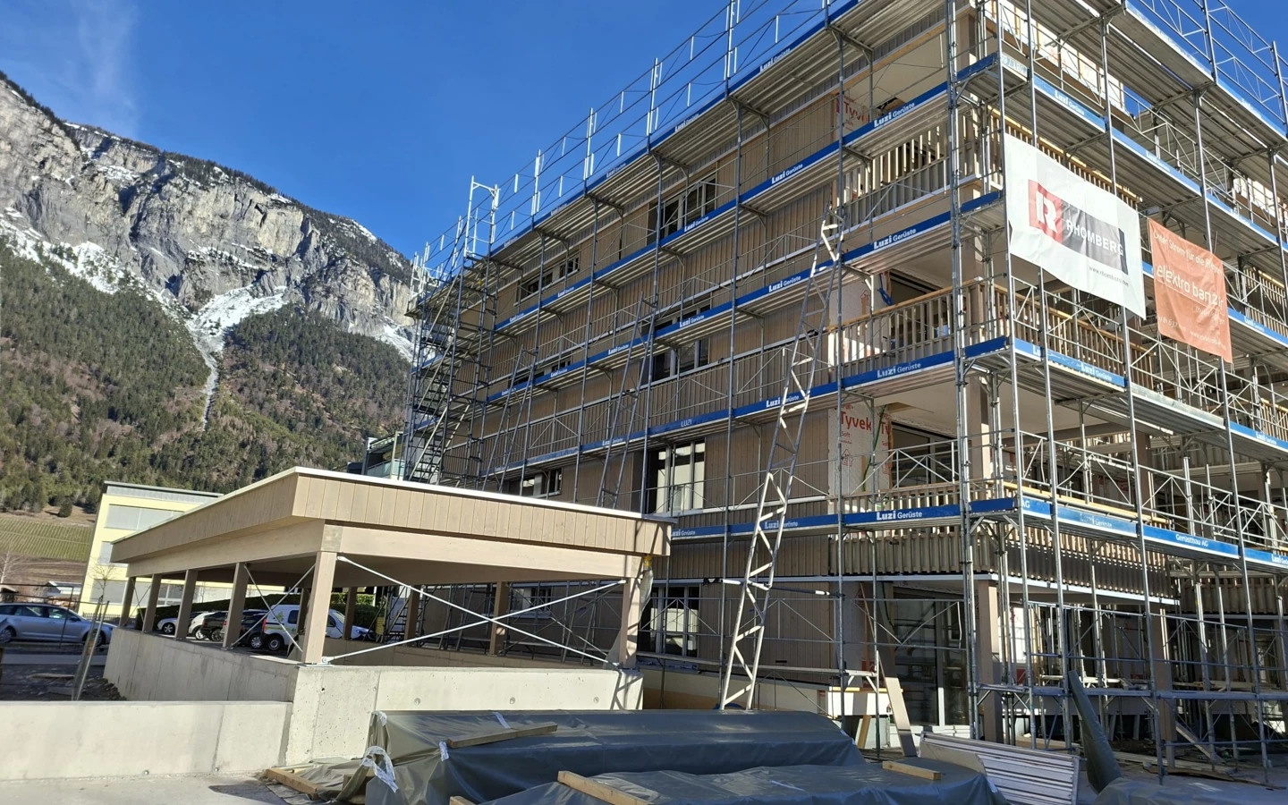 Holzbau-Mehrfamilienhaus in Domat/Ems mit Gerüst vor alpiner Bergkulisse