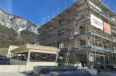 Holzbau-Mehrfamilienhaus in Domat/Ems mit Gerüst vor alpiner Bergkulisse