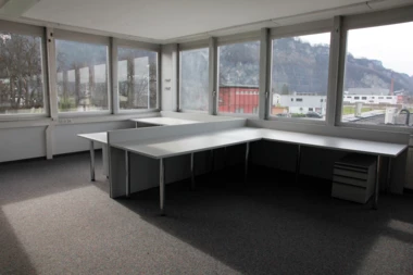 Leeres Eckbüro im Froschweg mit langen Schreibtischen, Fenstern mit Bergblick und Spannteppichboden (Büro).