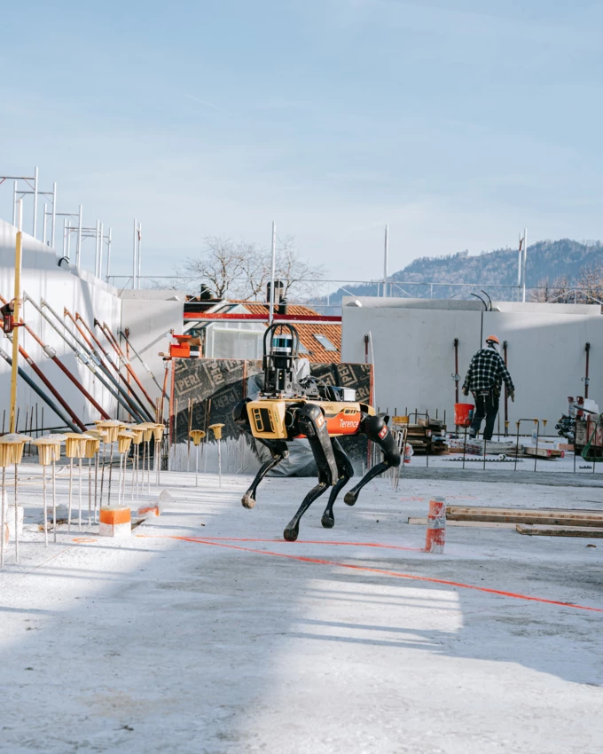 Ein gelb-schwarzer Roboterhund mit «Terrence»-Schriftzug auf einer Baustelle mit Bauarbeiter im Hintergrund.