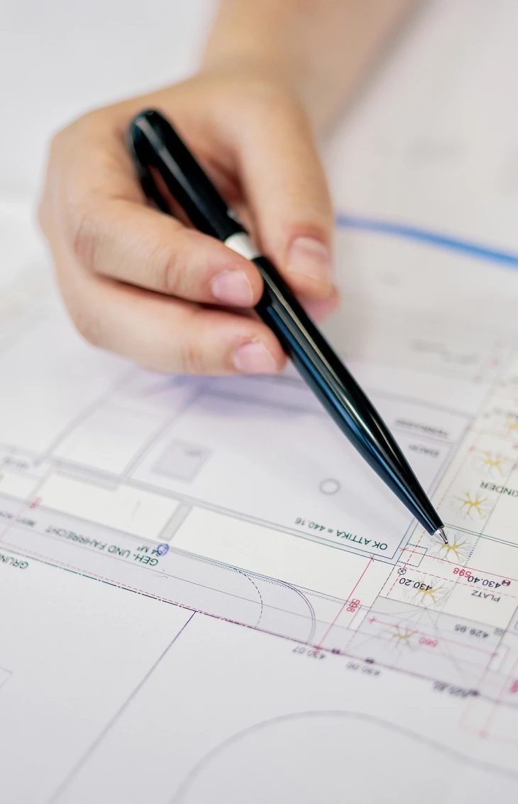 A hand holding a black pen points to details on a finely-tuned architectural blueprint document (planning, ideas)
