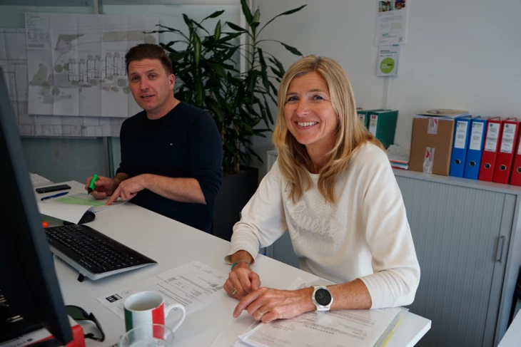 Lisa Ehrat wie sie an einem Schreibtisch mit einem Mann sitzt und in die Kamera lächelt Lisa Ehrat wie sie an einem Schreibtisch mit einem Mann sitzt und in die Kamera lächelt