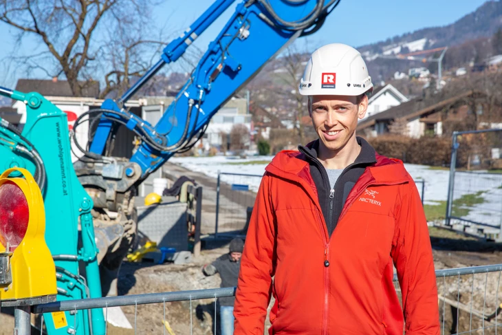 Florian Egle steht vor Bagger auf Baustelle für Web Florian Egle steht vor Bagger auf Baustelle für Web