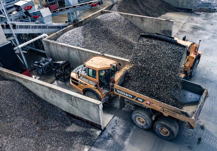 Ein gelber Volvo Radlader bewegt Schotter in einen gelben Volvo Lkw (Steinbruch).