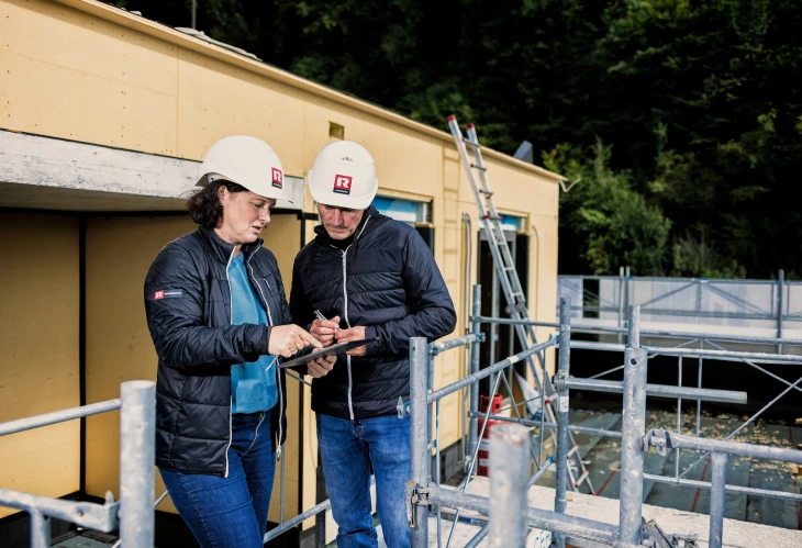 Zwei Bauleiter in Rhomberg Bau Helmen besprechen Pläne auf einem Tablet auf der Baustelle (besprechung, Bauleiterin).