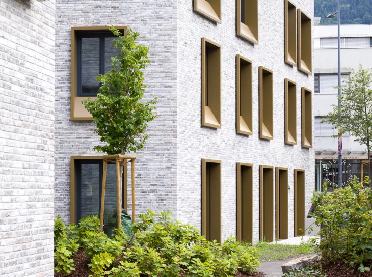 Umfassungsmauer und modernes Gebäude aus hellen Ziegeln an der Kreuzgasse Dornbirn mit Goldfenstern und einem gepflegten Garten