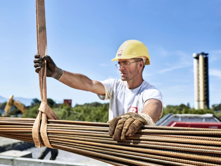 Hochbau Rhomberg Bau Mann hält Kranseil mit Metallstangen daran