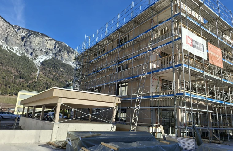 Holzbau-Mehrfamilienhaus in Domat/Ems mit Gerüst vor alpiner Bergkulisse