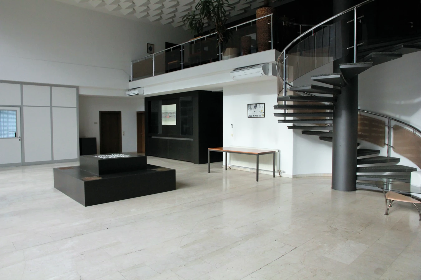 Modernes Bürointerieur mit hellem Marmorboden, einer Wendeltreppe zum Obergeschoss und einer Bar im Hintergrund (Froschweg, Büro).