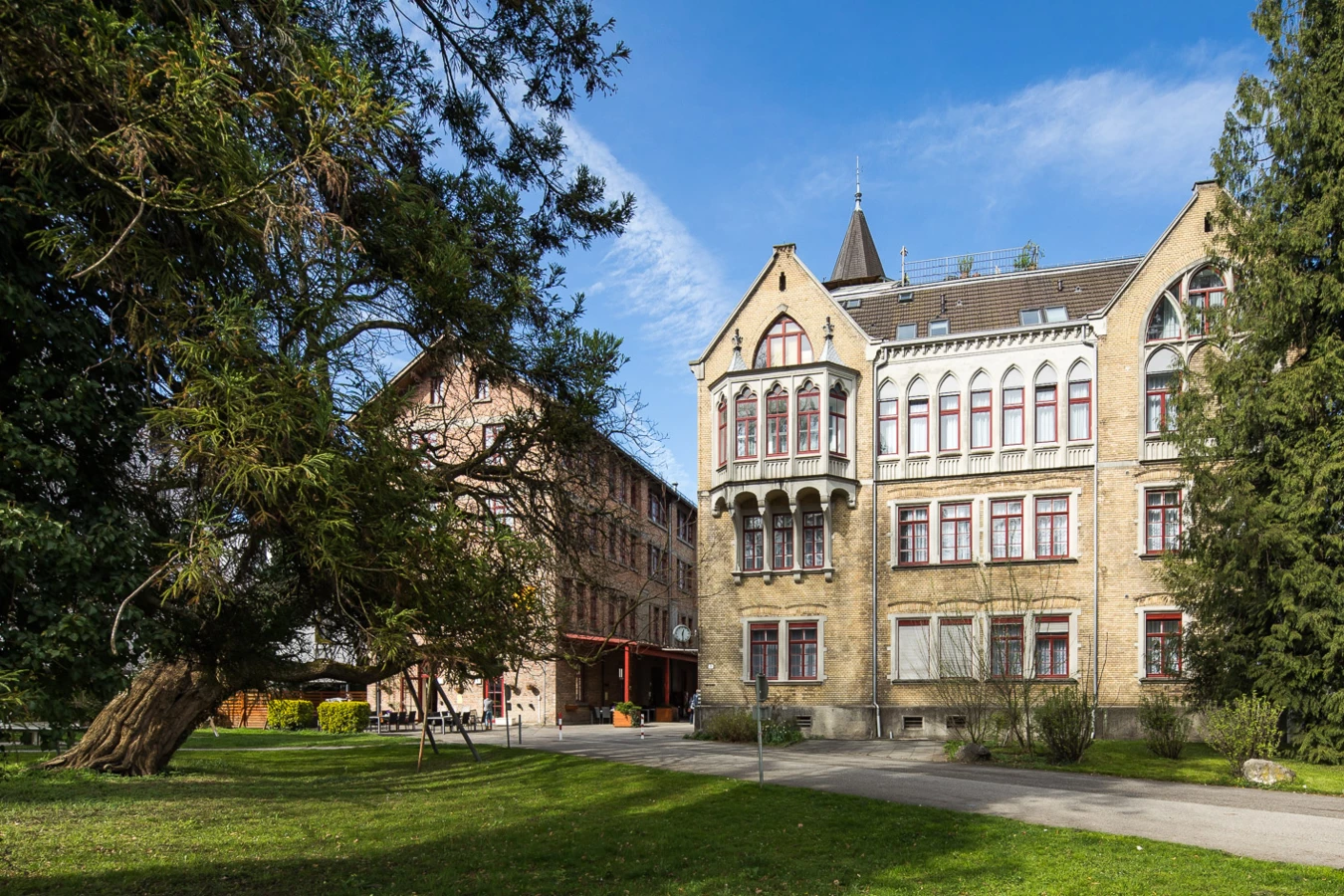 Zwei historische Gebäude am Benger Areal mit einem alten Baum im Vordergrund und blauem Himmel
